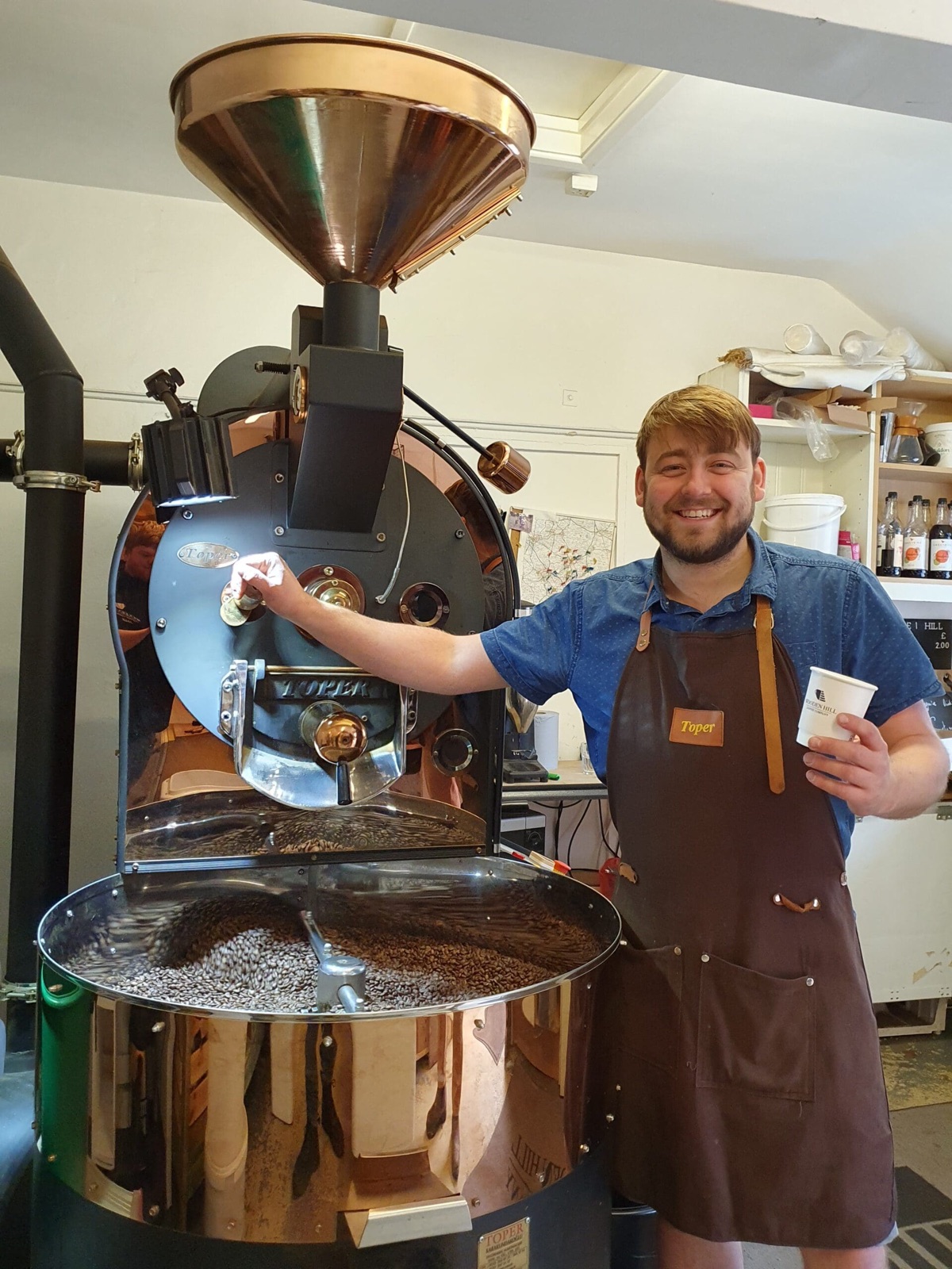 A roaster at Wooden Hill Coffee Company beside their copper roasting machine